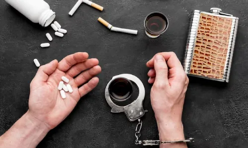 Pills, a hip flask and handcuffs beside a person’s hands