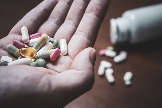 An open hand holding many tablets and capsules