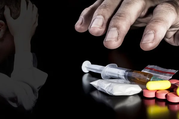 A person holding their head in their hands beside drugs and pills