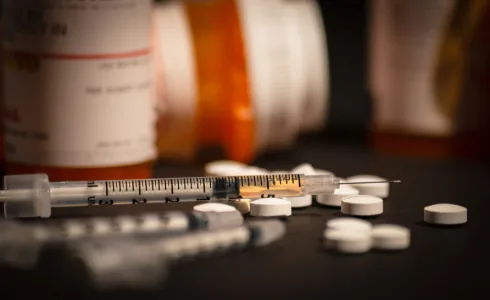 A syringe and scattered pills on a dark surface